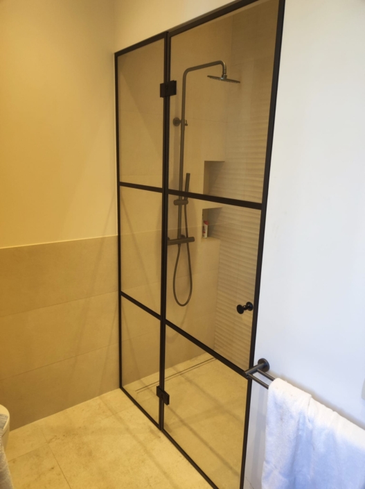 Installation de parois de douche en verre sur-mesure style atelier avec profils noirs dans un hôtel particulier à Nice.